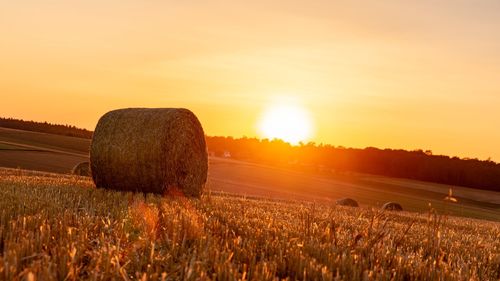 Hay bales on field against sky during sunset