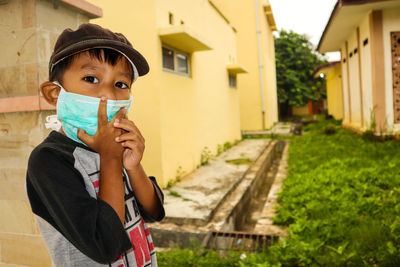 Portrait of boy wearing pollution mask while standing on sidewalk