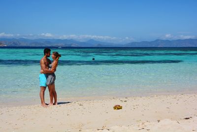 Young couple standing on beach against sky