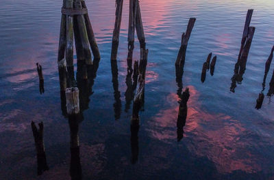 Reflection of wooden posts in lake against sky