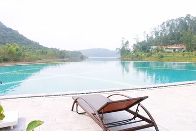 Chairs and tables by swimming pool against sky