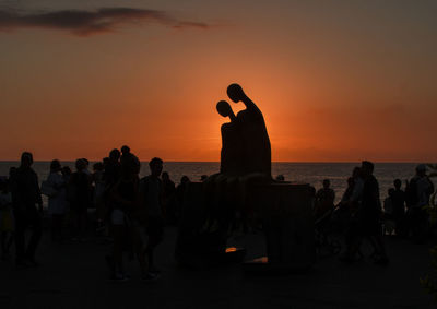 Silhouette people on beach against sky during sunset