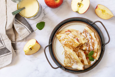 Homemade sweet crepes with apples and condensed milk on a marble tabletop. top view flat lay.