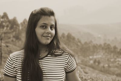 Portrait of smiling young woman standing against landscape