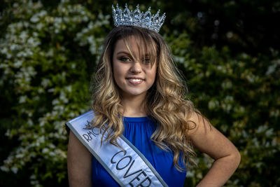 Portrait of smiling young woman wearing crown standing against plants