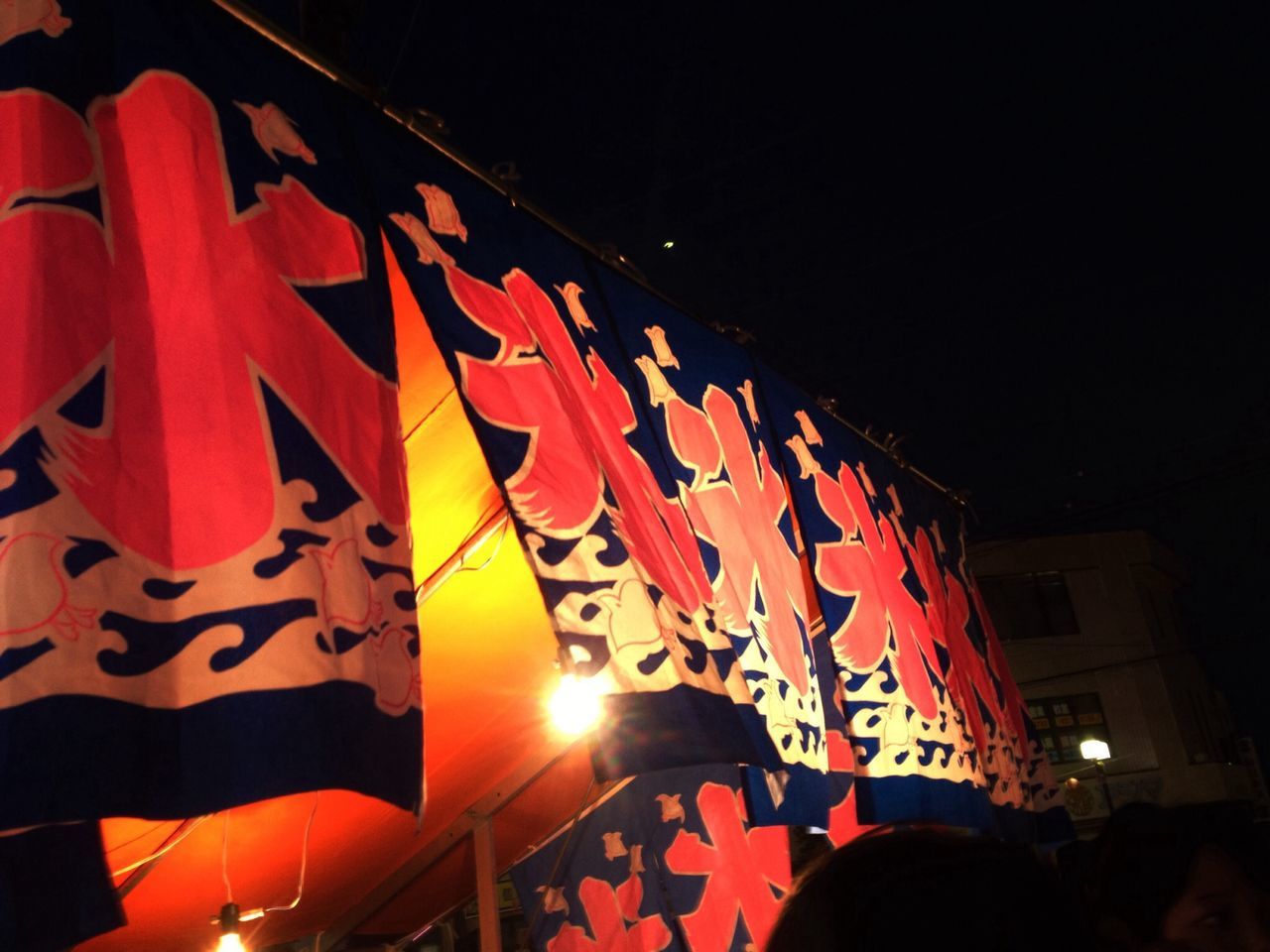 red, low angle view, built structure, illuminated, sunlight, night, flag, architecture, no people, text, outdoors, building exterior, patriotism, sky, multi colored, hanging, orange color, tradition, cultures, decoration