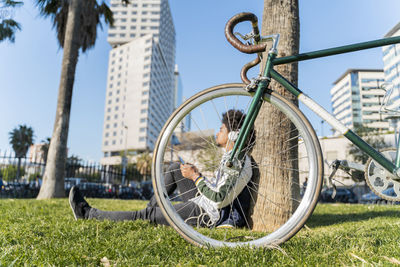 Casual businessman with bicycle taking a break in urban park listening to music, barcelona, spain