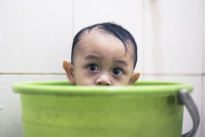 Close-up of boy in green bucket against tile wall at bathroom