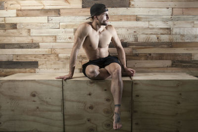 Full length of shirtless man sitting on wood