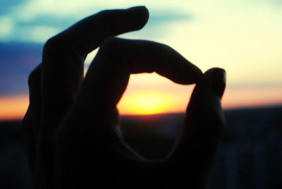 Midsection of person holding heart shape against sky during sunset