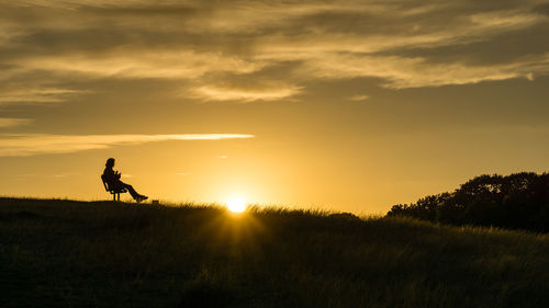 Person sitting on field against sky during sunset