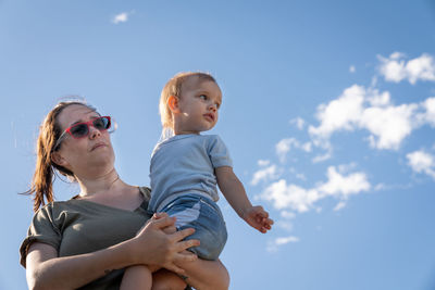 Mother with her baby daughter in her arms with illuminated sky background with white clouds