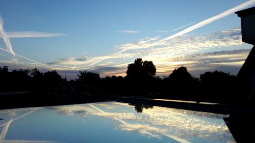 Silhouette trees by swimming pool against sky during sunset