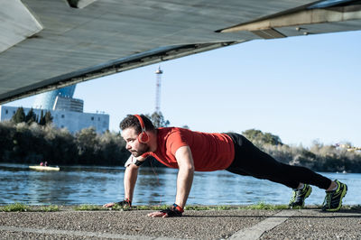 Full length of man listening music while doing push-ups against lake