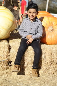 Full length portrait of a smiling boy with pumpkins on field