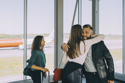 Smiling businesswoman looking at colleagues greeting while standing in airport corridor