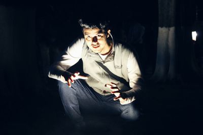 Portrait of man crouching in forest at night