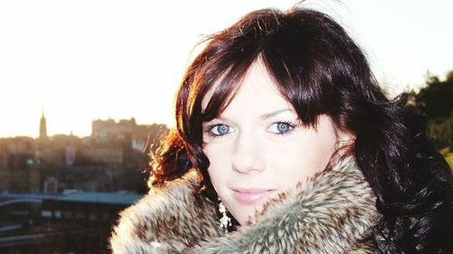 Portrait of beautiful smiling woman wearing fake fur standing against cityscape