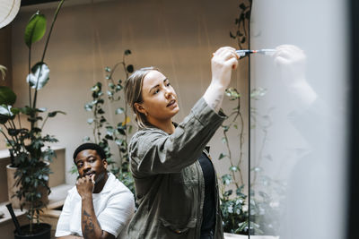 Female entrepreneur writing business strategy on whiteboard while explaining to colleagues in office