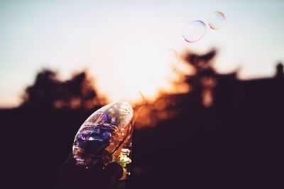 Cropped image of silhouette person holding bubble gun during sunset