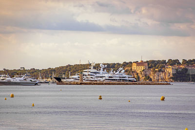 Sailboats in sea by buildings in city against sky