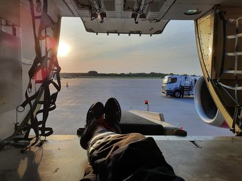 Low section of man in cargo hold against sky during sunset