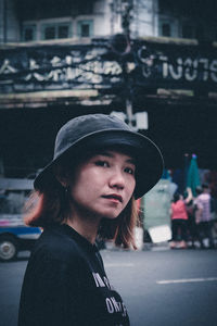 Portrait of young woman looking away while standing on street in city