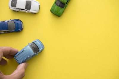 Cropped hand holding toy car against yellow background