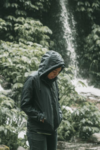 Young man standing against waterfall in forest