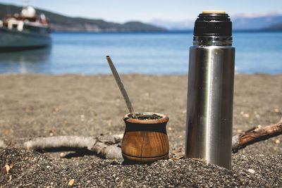 Close-up of water bottle with bowl on sand at beach