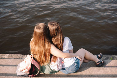 Back view of lesbian couple embracing while sitting on steps by river