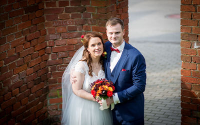 Bride and groom standing by brick wall