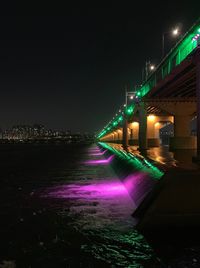 Illuminated bridge over river amidst buildings against sky at night