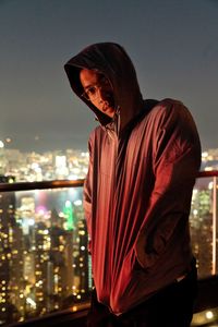 Portrait of young man standing against illuminated city at night