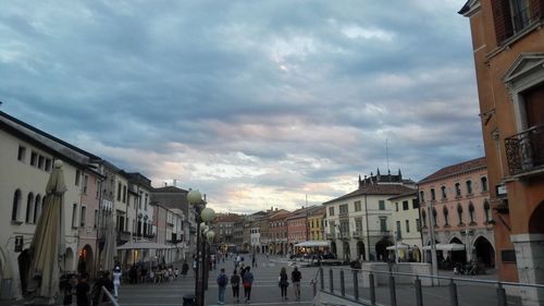 People walking on street amidst buildings in city against sky