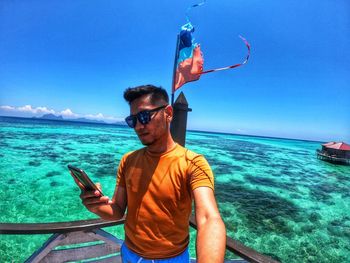 Young man using mobile phone in sea against sky