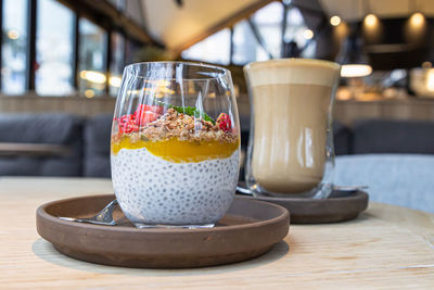 Chia pudding with mango puree, oats flakes and strawberries and cappuccino on table in cafe