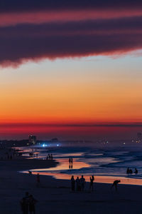 Silhouette people on beach against orange sky