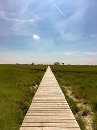 Wooden footpath amidst field against sky