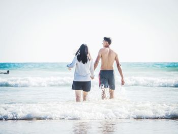 Rear view of couple walking in sea against clear sky