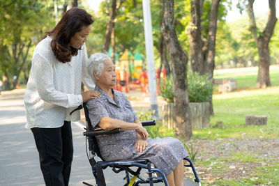 Caregiver help and care asian senior woman patient sitting and happy on wheelchair in park