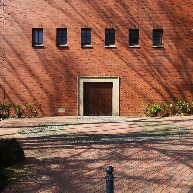 building exterior, architecture, built structure, brick wall, house, window, wall - building feature, street, cobblestone, wall, outdoors, day, sidewalk, sunlight, building, potted plant, shadow, footpath, residential structure, residential building