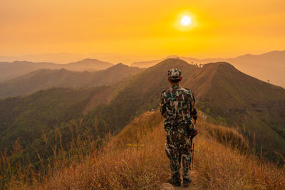 Rear view of man standing on mountain against sky during sunset