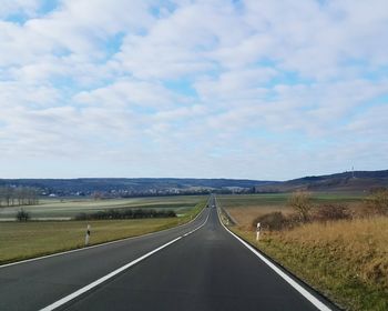 Empty road amidst field against sky