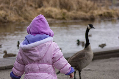 Rear view of baby girl wearing warm clothing standing against lake