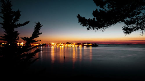 Silhouette trees by sea against sky at sunset