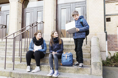 Schoolgirls looking at boy holding laptop on steps