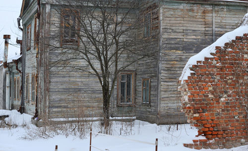 Snow covered house against bare trees during winter