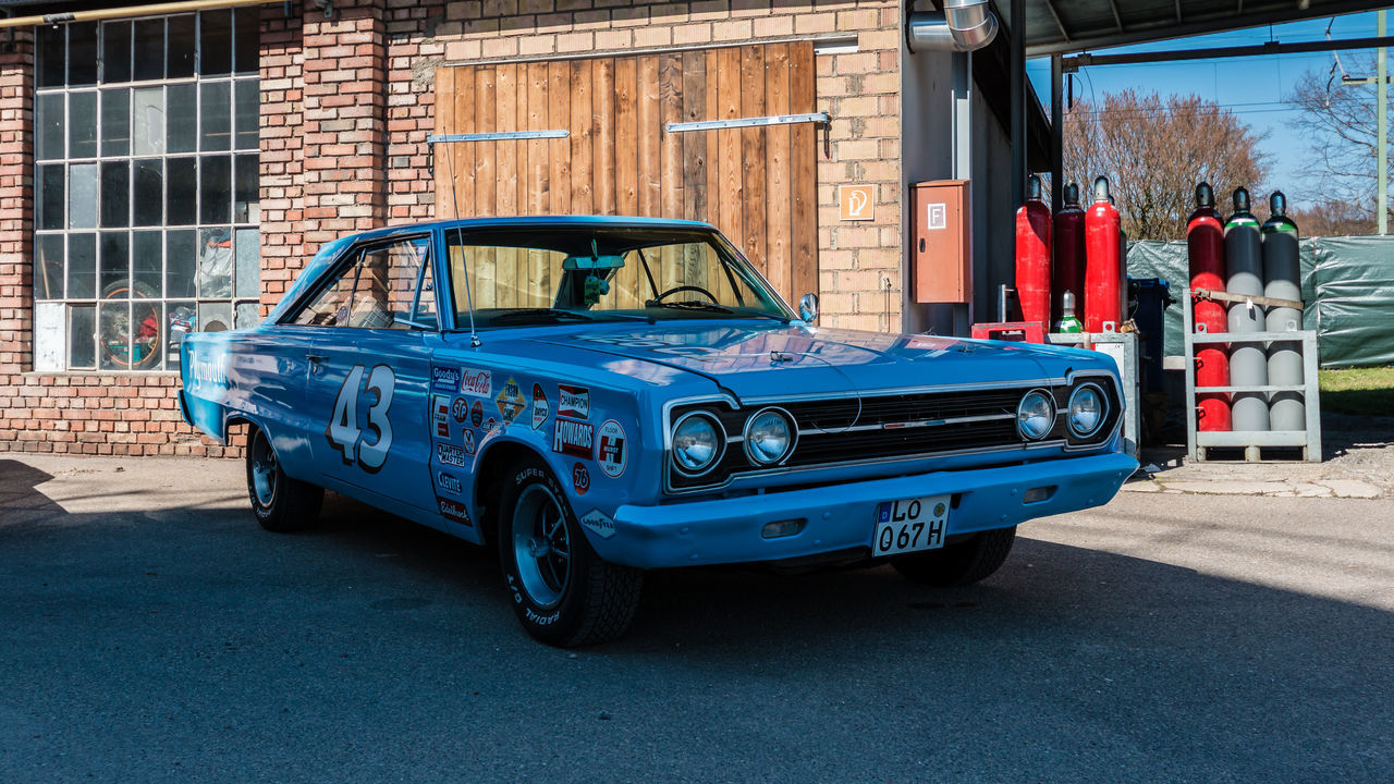 mode of transportation, transportation, car, motor vehicle, architecture, land vehicle, building exterior, built structure, blue, day, city, road, vintage car, street, retro styled, outdoors, no people, building, travel, garage