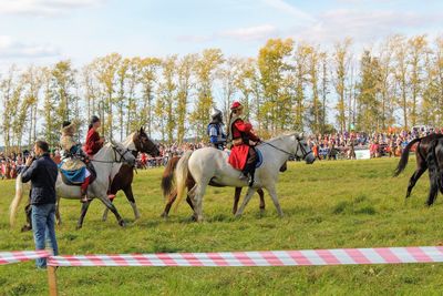 People riding horses on field against sky